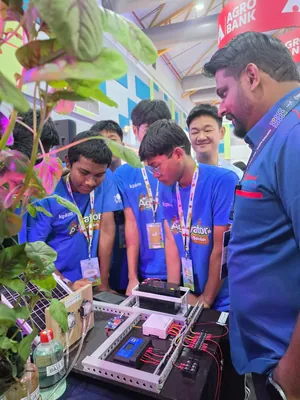 Students looking closely at a control panel prototype with dosing pumps and a solar panel