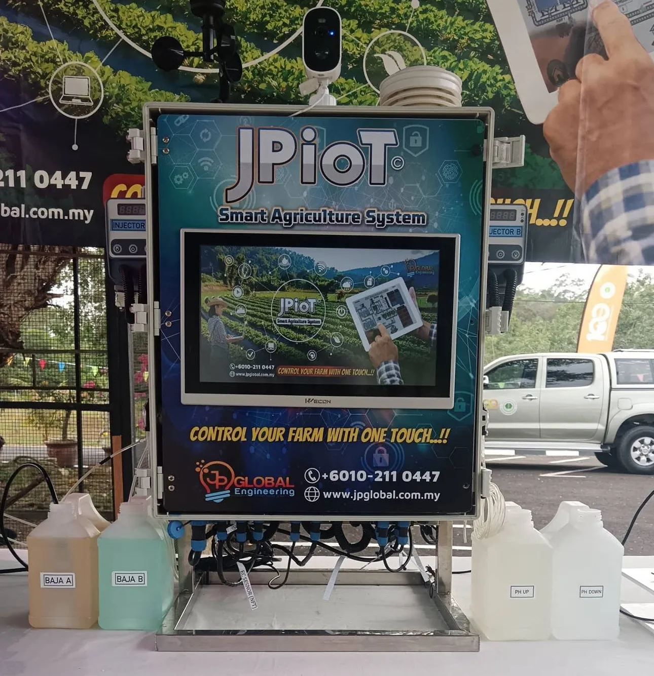 A JPiOT controller on a demonstration table, with dosing pumps labelled Injector A and Injector B on either side and four containers labelled Baja A, Baja B, pH up and pH down in front